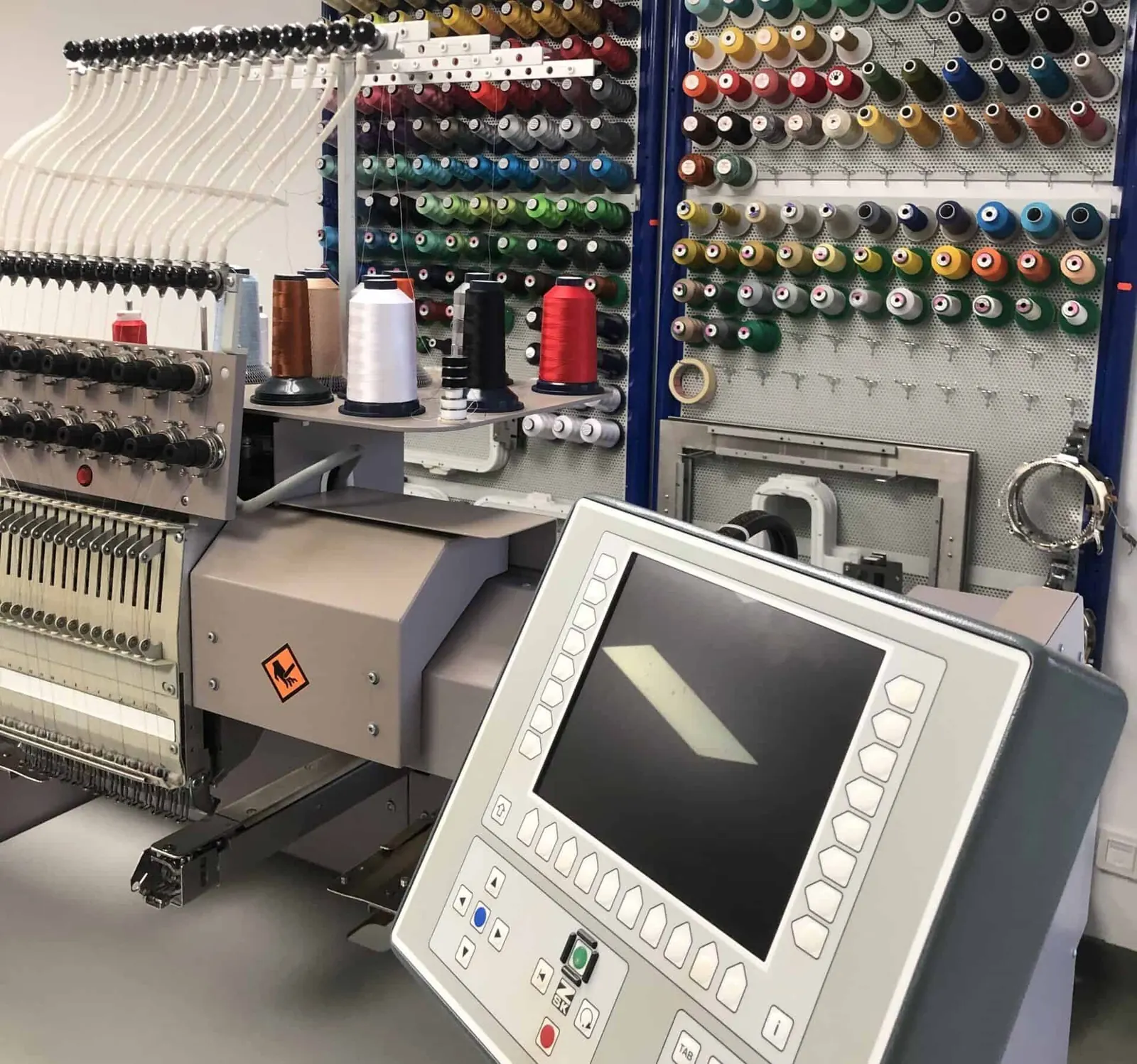 Stickmaschine und Garnwand mit Dutzenden Garnfarben in der Werkstatt von 1aShirt in Emden