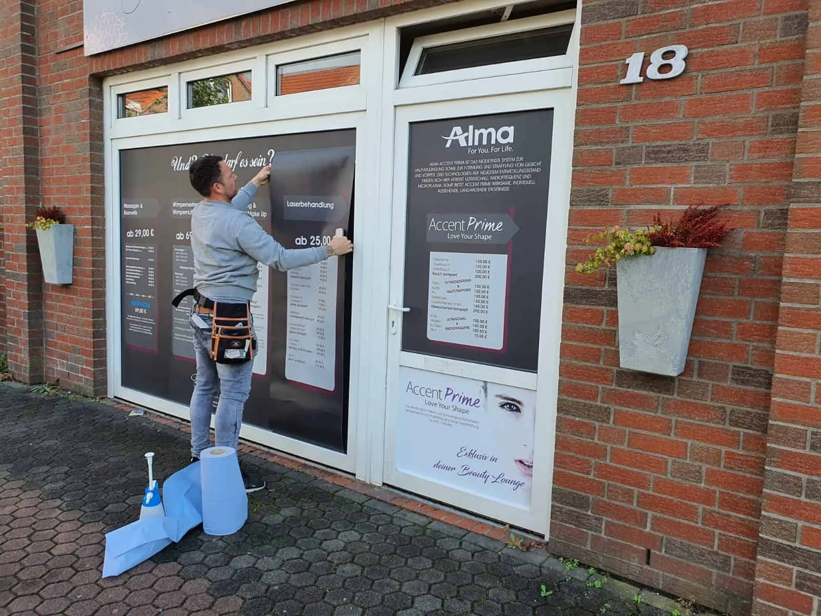 Mitarbeiter von 1aShirt bringt eine Schaufensterbeschriftung an einer Ladenfront aus rotem Klinker an