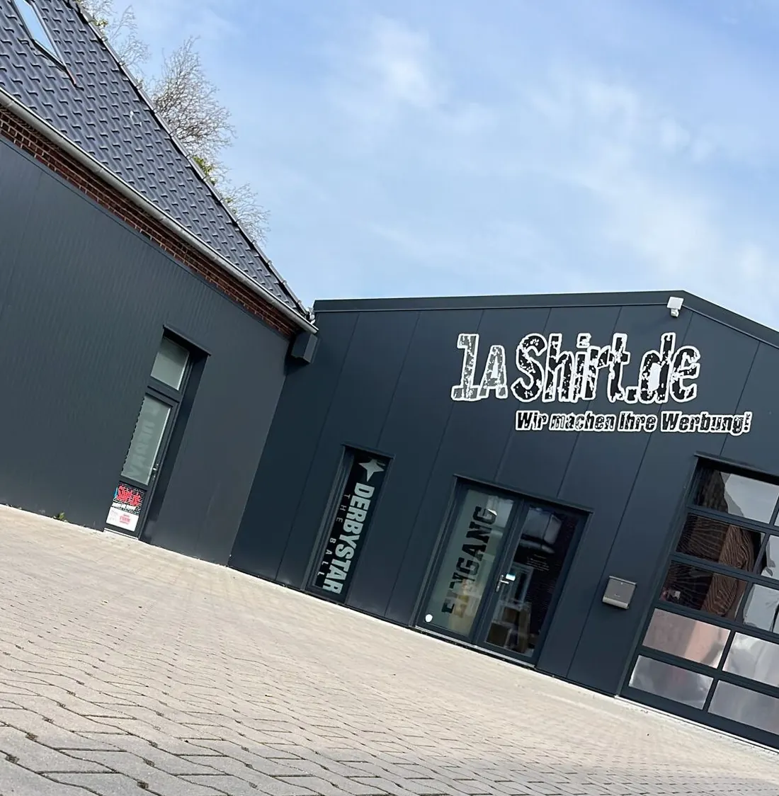 Werkstattgebäude von 1aShirt an der Auricher Straße 128 in Emden mit beschrifteter Fassade