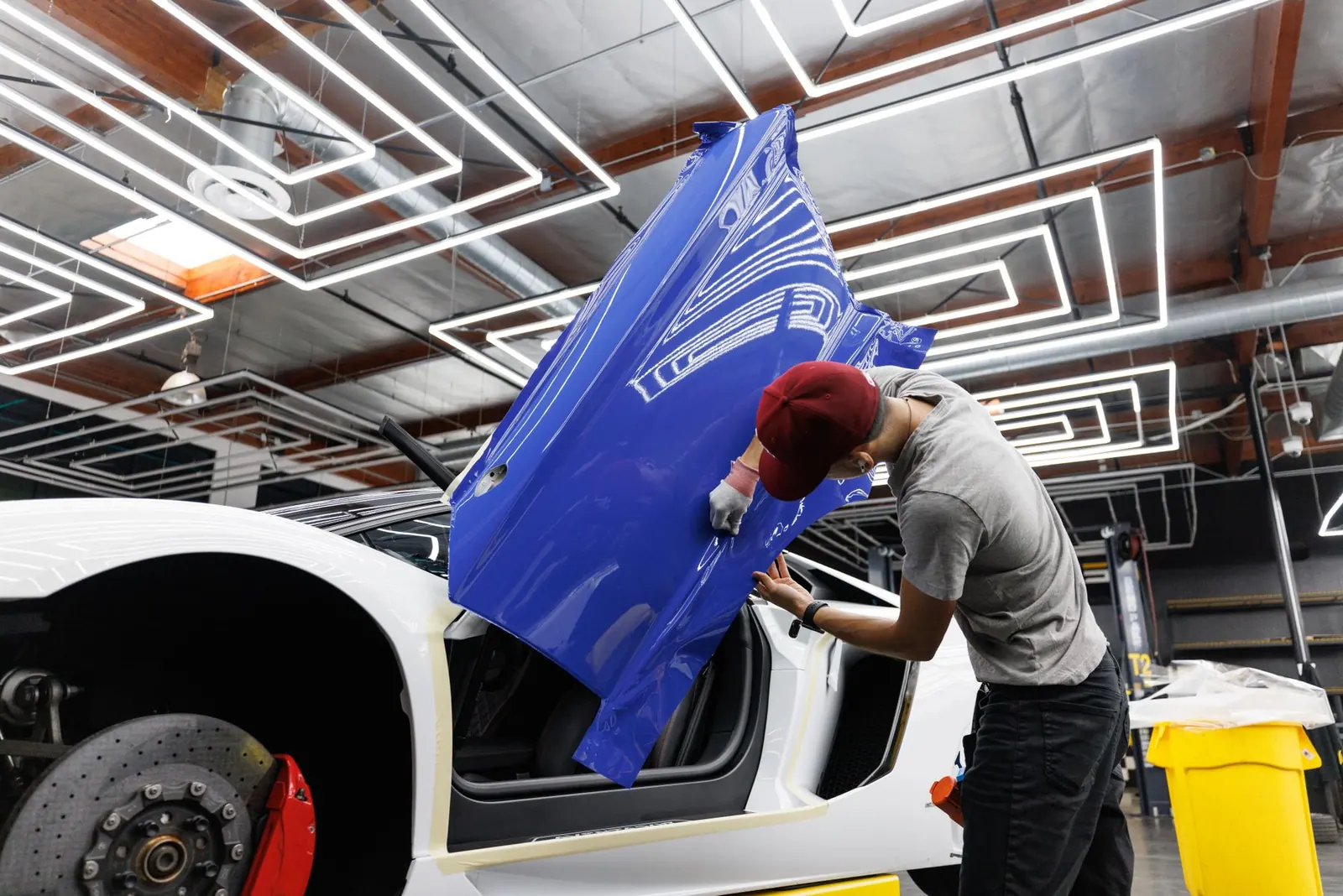 Folierer legt eine blaue Fahrzeugfolie an eine Autotür in einer Werkstatt