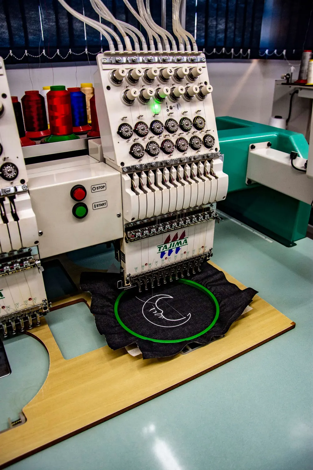 Stickmaschine mit eingespanntem Stickrahmen und dunklem Textil, auf dem ein Logo gestickt wird