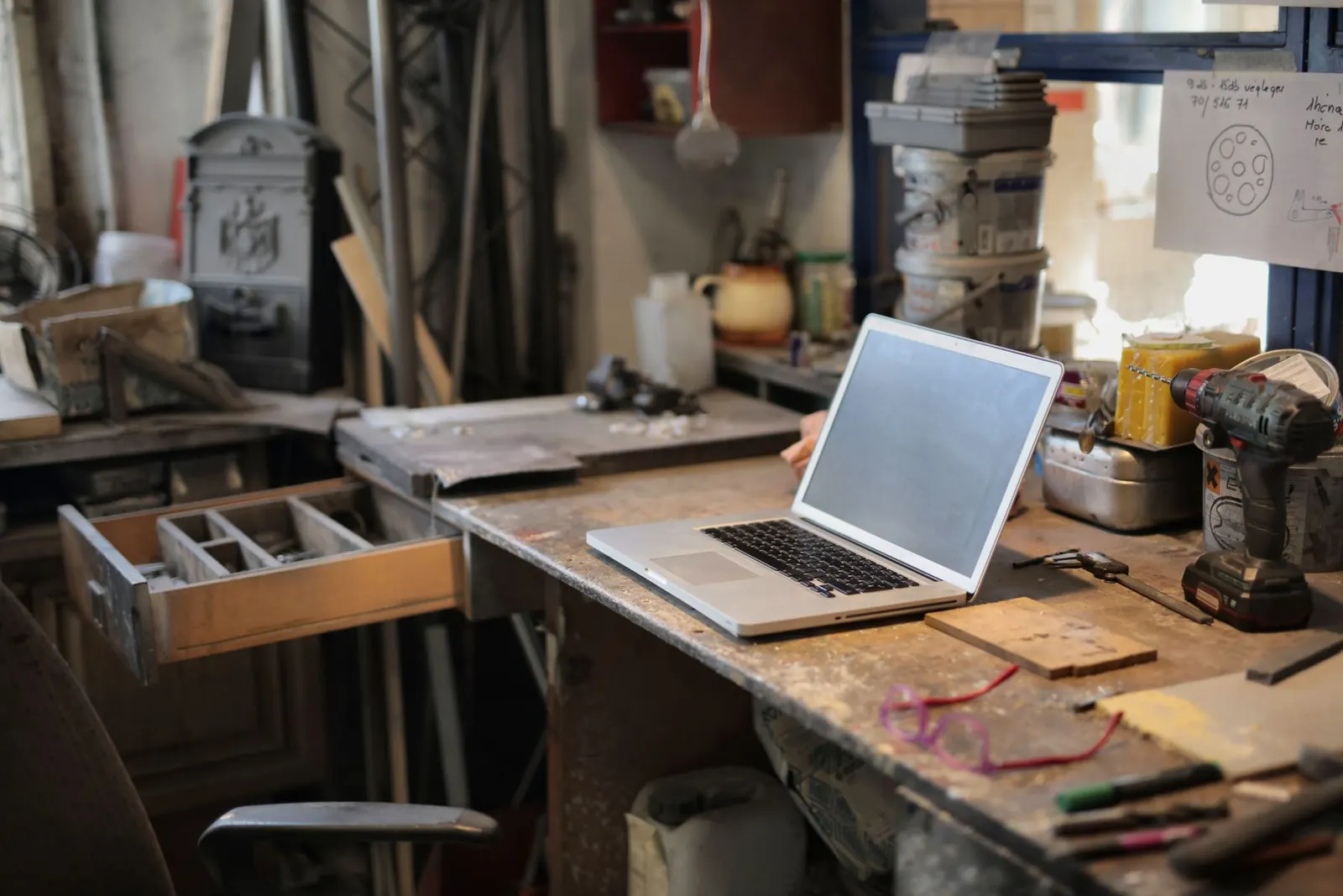 Aufgeklappter Laptop auf einer Werkbank zwischen Werkzeug und Zeichnungen